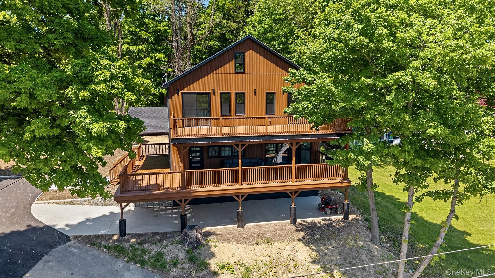 Contemporary brown siding residence featuring a multi-level deck system with wood railings, a covered patio area, and a paved driveway Contemporary brown siding residence featuring a multi-level deck system with wood railings, a covered patio area, and a paved driveway