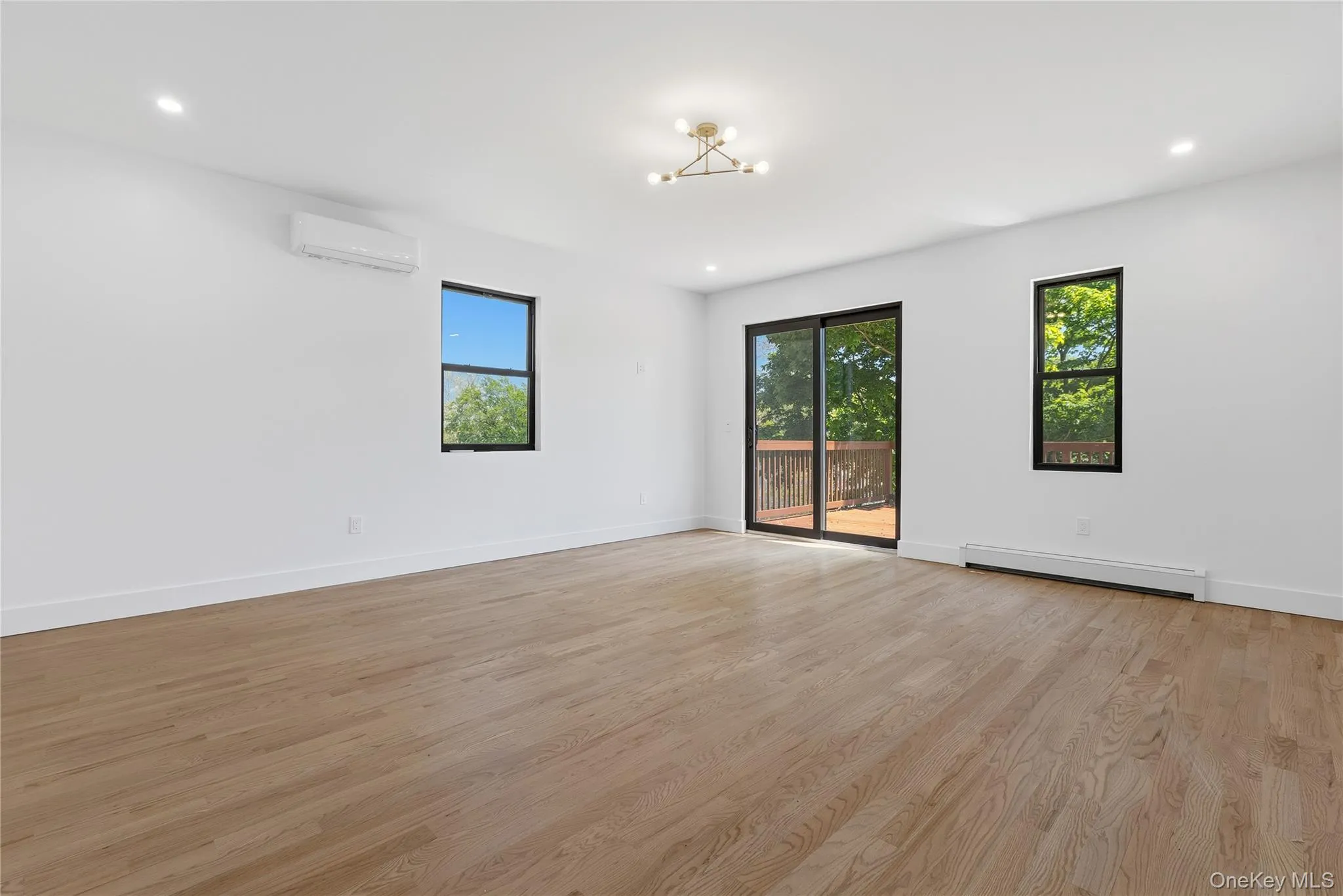 Spacious room featuring wood-finish flooring, white walls, and a contemporary ceiling light fixture Spacious room featuring wood-finish flooring, white walls, and a contemporary ceiling light fixture