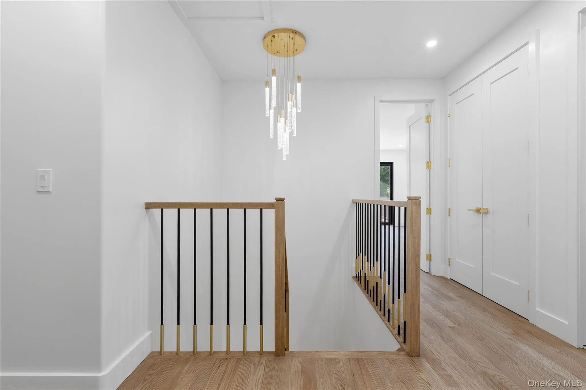 Upper hallway featuring a contemporary chandelier, light wood-finish flooring, and white paneled doors with gold-finish hardware Upper hallway featuring a contemporary chandelier, light wood-finish flooring, and white paneled doors with gold-finish hardware