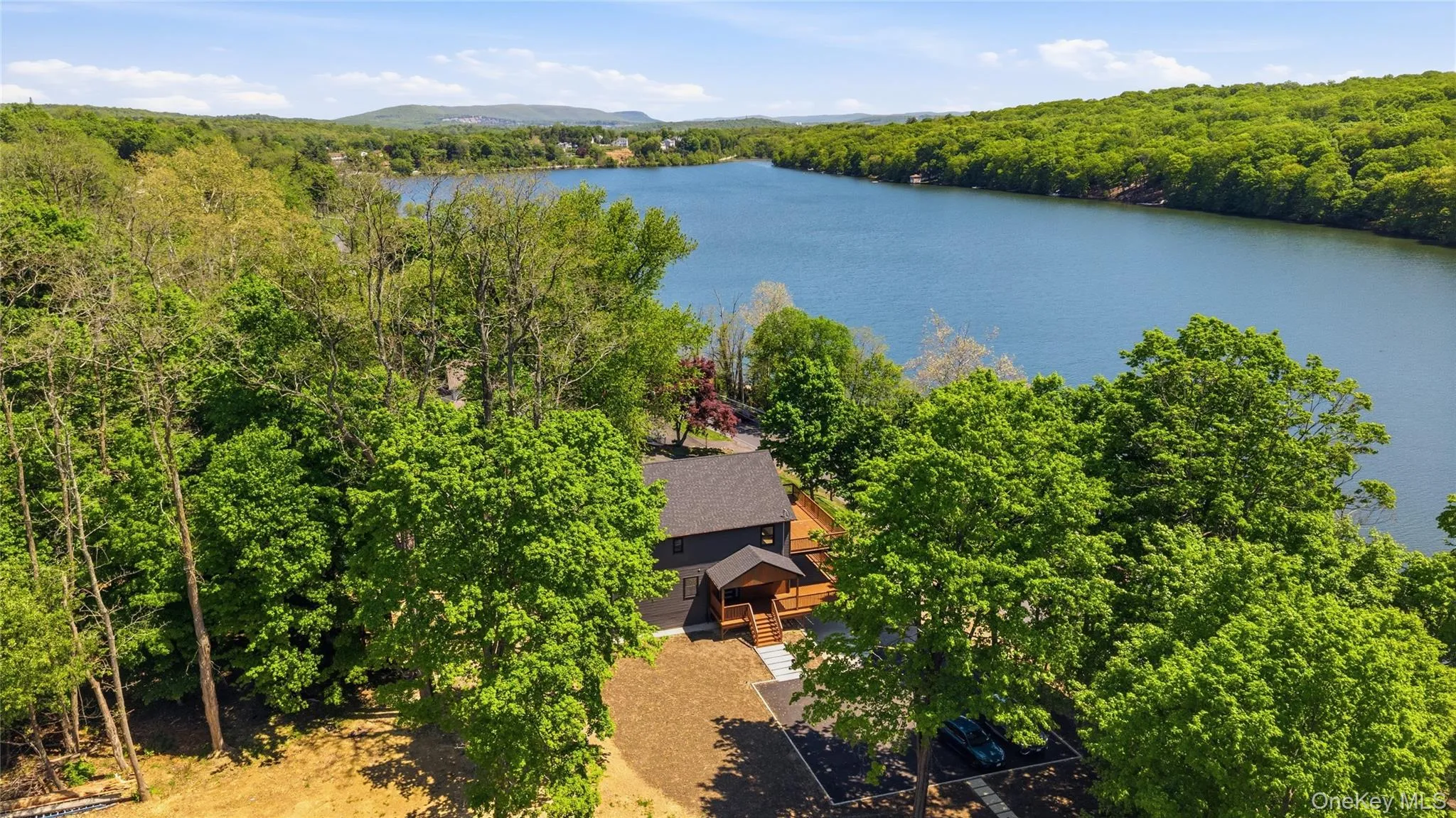 Modern lakeside residence featuring a dark-toned exterior, a natural wood-finish deck, and a paved parking area Modern lakeside residence featuring a dark-toned exterior, a natural wood-finish deck, and a paved parking area