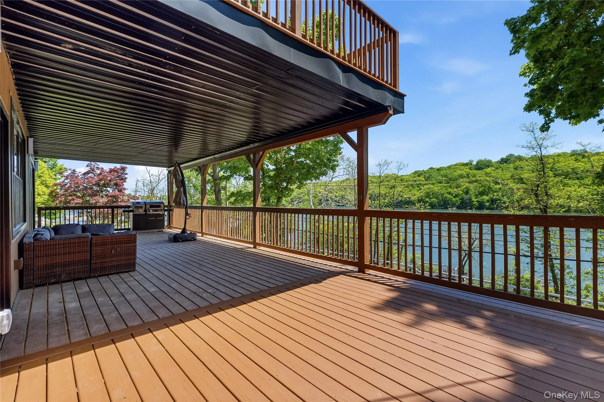 Expansive wood-finish deck with a solid wood railing system, offering clear sightlines to the surrounding trees and body of water Expansive wood-finish deck with a solid wood railing system, offering clear sightlines to the surrounding trees and body of water