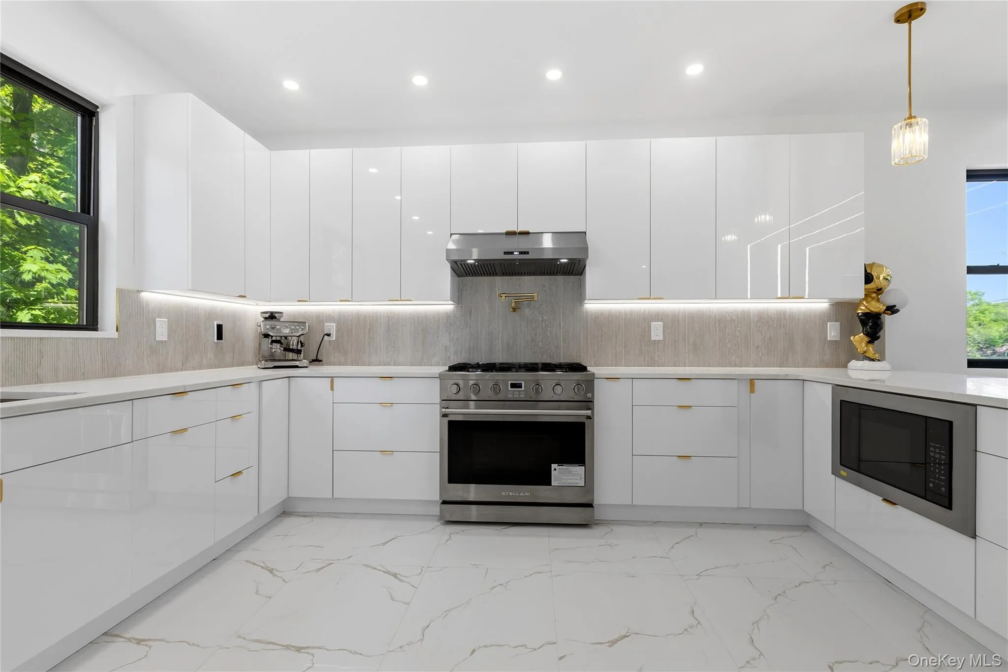 Contemporary kitchen featuring white high-gloss cabinetry, stainless steel range with matching hood, integrated microwave, and undermount lighting above a light-toned backsplash Contemporary kitchen featuring white high-gloss cabinetry, stainless steel range with matching hood, integrated microwave, and undermount lighting above a light-toned backsplash