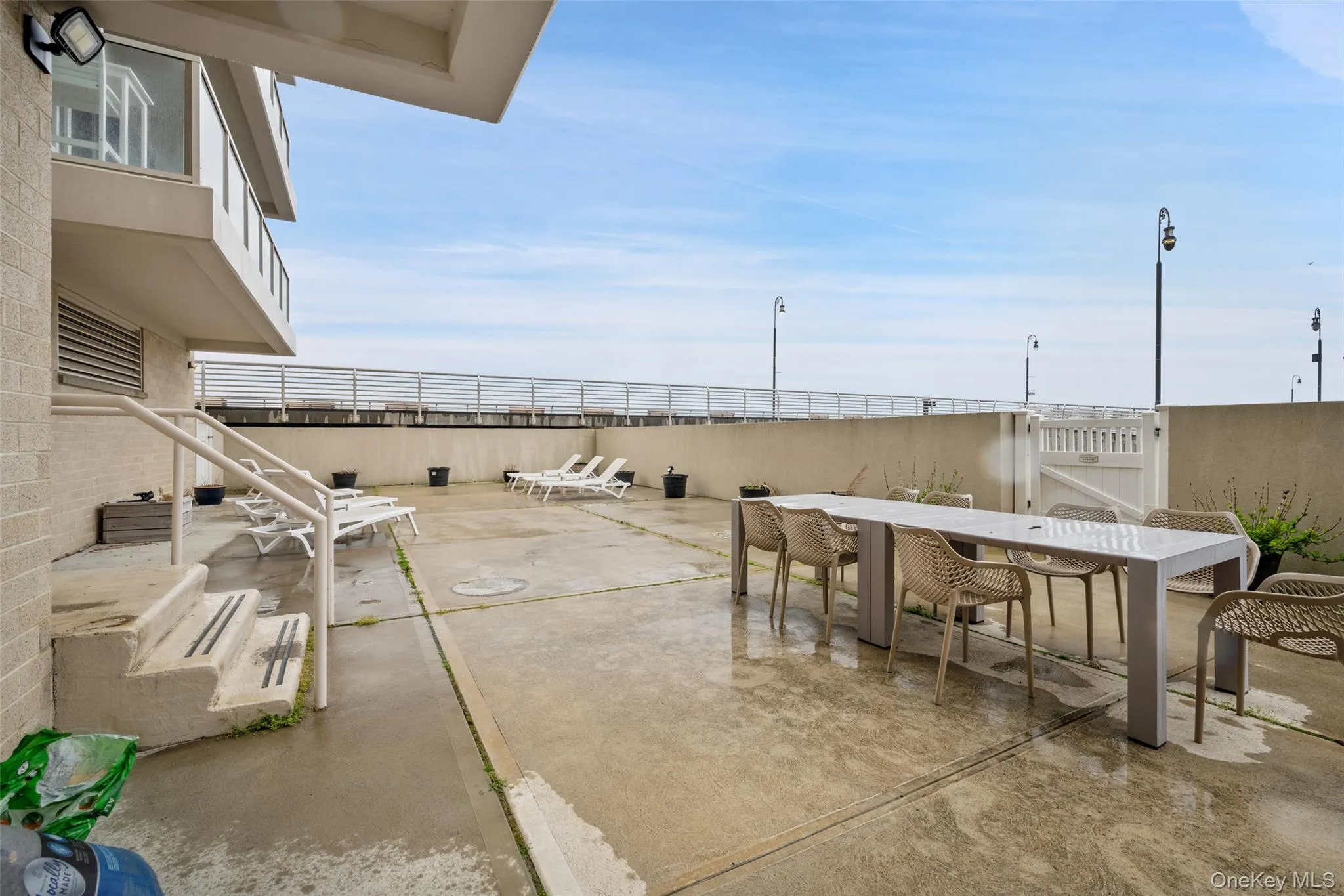 Expansive patio area featuring concrete paving, a perimeter wall, and a white access gate Expansive patio area featuring concrete paving, a perimeter wall, and a white access gate