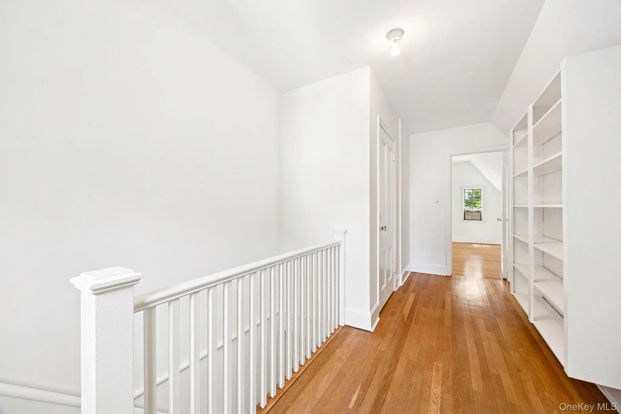 Hallway with an upstairs landing, light wood-style floors, and lofted ceiling Hallway with an upstairs landing, light wood-style floors, and lofted ceiling