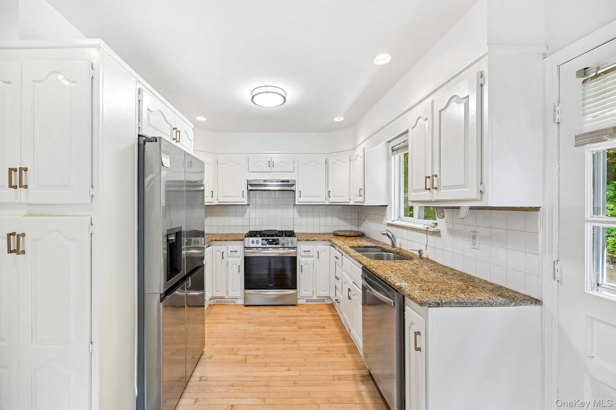 Kitchen featuring stainless steel appliances, backsplash, light wood-style flooring, white cabinetry, and recessed lighting Kitchen featuring stainless steel appliances, backsplash, light wood-style flooring, white cabinetry, and recessed lighting