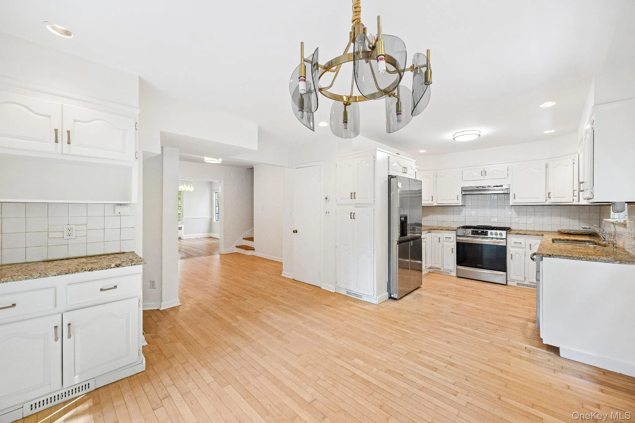 Kitchen featuring decorative backsplash, a chandelier, recessed lighting, light wood-style floors, and appliances with stainless steel finishes Kitchen featuring decorative backsplash, a chandelier, recessed lighting, light wood-style floors, and appliances with stainless steel finishes
