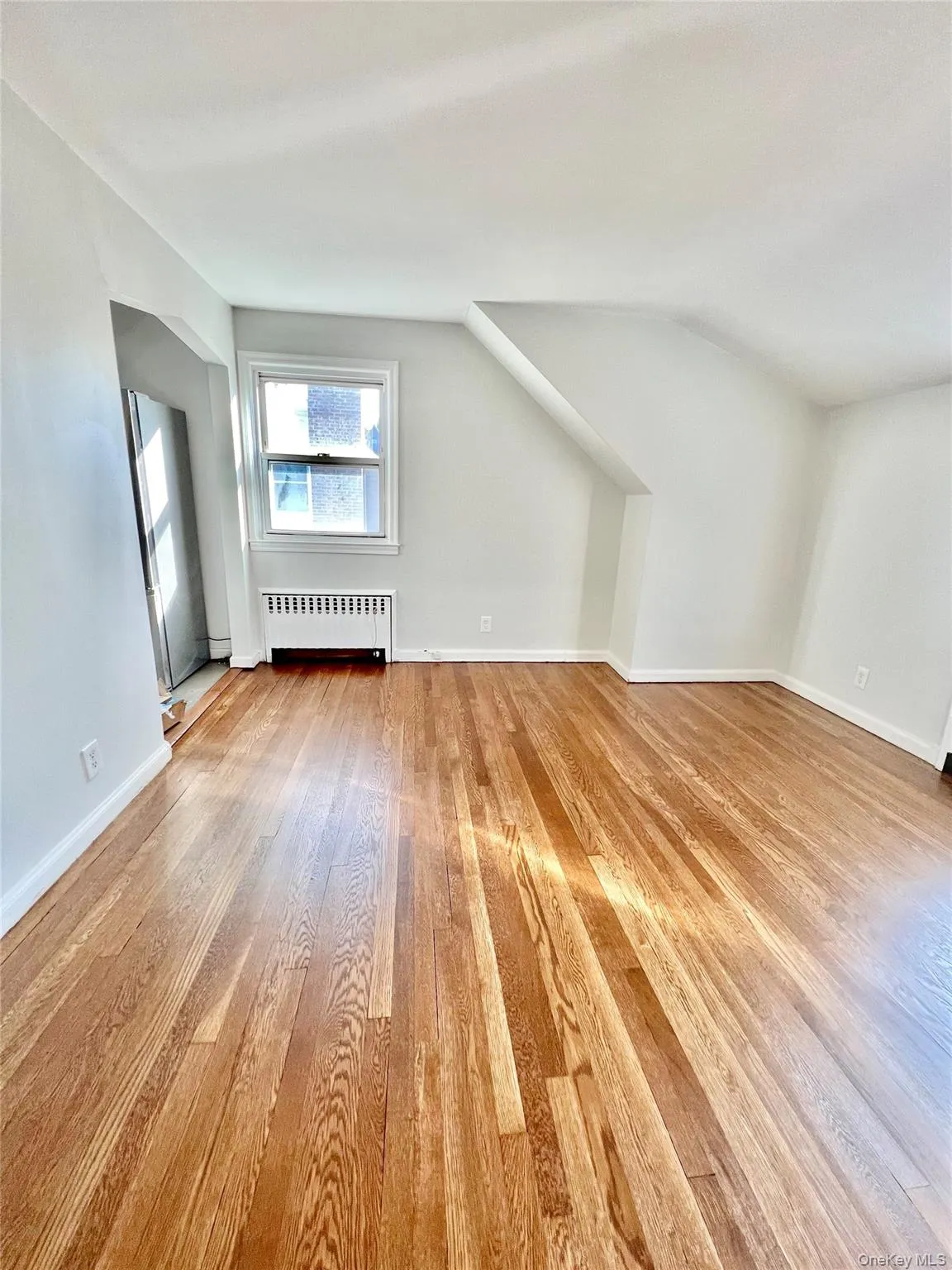 Hardwood flooring throughout the living room featuring a window with white trim, a baseboard radiator, and white painted walls Hardwood flooring throughout the living room featuring a window with white trim, a baseboard radiator, and white painted walls