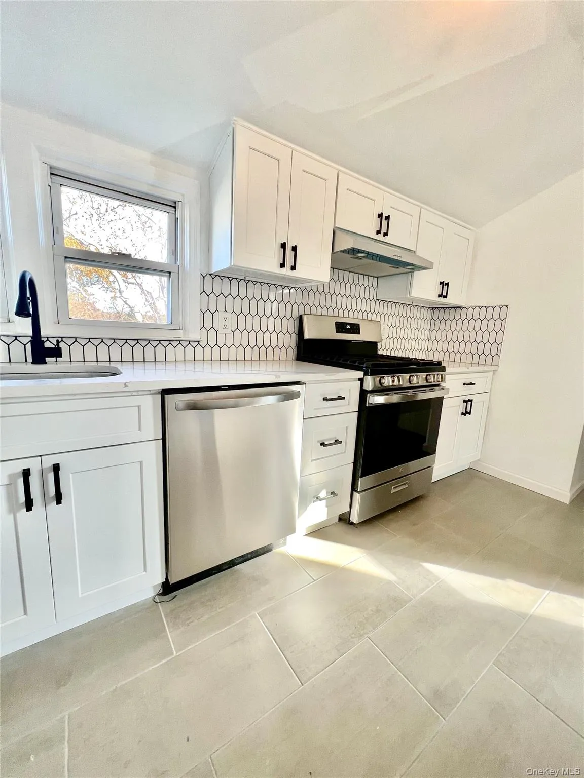 Kitchen featuring white shaker cabinetry, stainless steel appliances, white countertops, a mosaic tile backsplash, and light-toned floor tiles Kitchen featuring white shaker cabinetry, stainless steel appliances, white countertops, a mosaic tile backsplash, and light-toned floor tiles