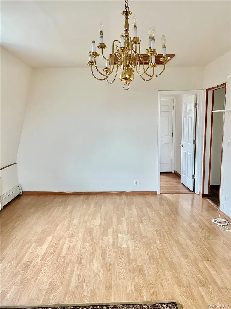 Spacious living room /main dining featuring wood-finish flooring, a brass chandelier, and white painted walls Spacious living room /main dining featuring wood-finish flooring, a brass chandelier, and white painted walls