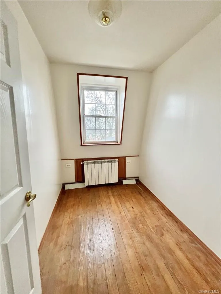 Hardwood flooring complements a white-painted room with a double-hung window, baseboard paneling, and a ceiling-mounted light fixture Hardwood flooring complements a white-painted room with a double-hung window, baseboard paneling, and a ceiling-mounted light fixture