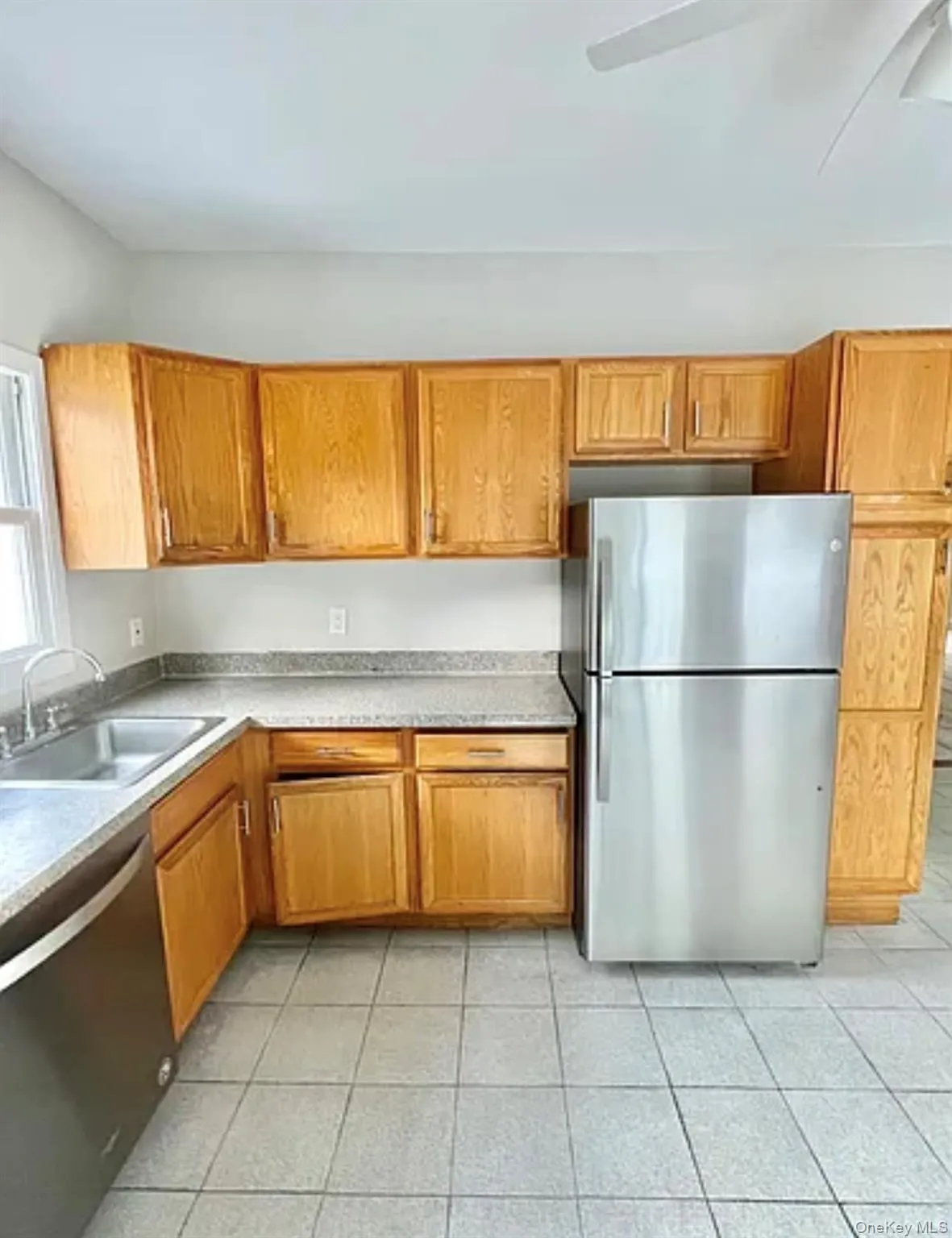Kitchen with wood cabinetry, light-toned countertops, and a stainless steel refrigerator Kitchen with wood cabinetry, light-toned countertops, and a stainless steel refrigerator