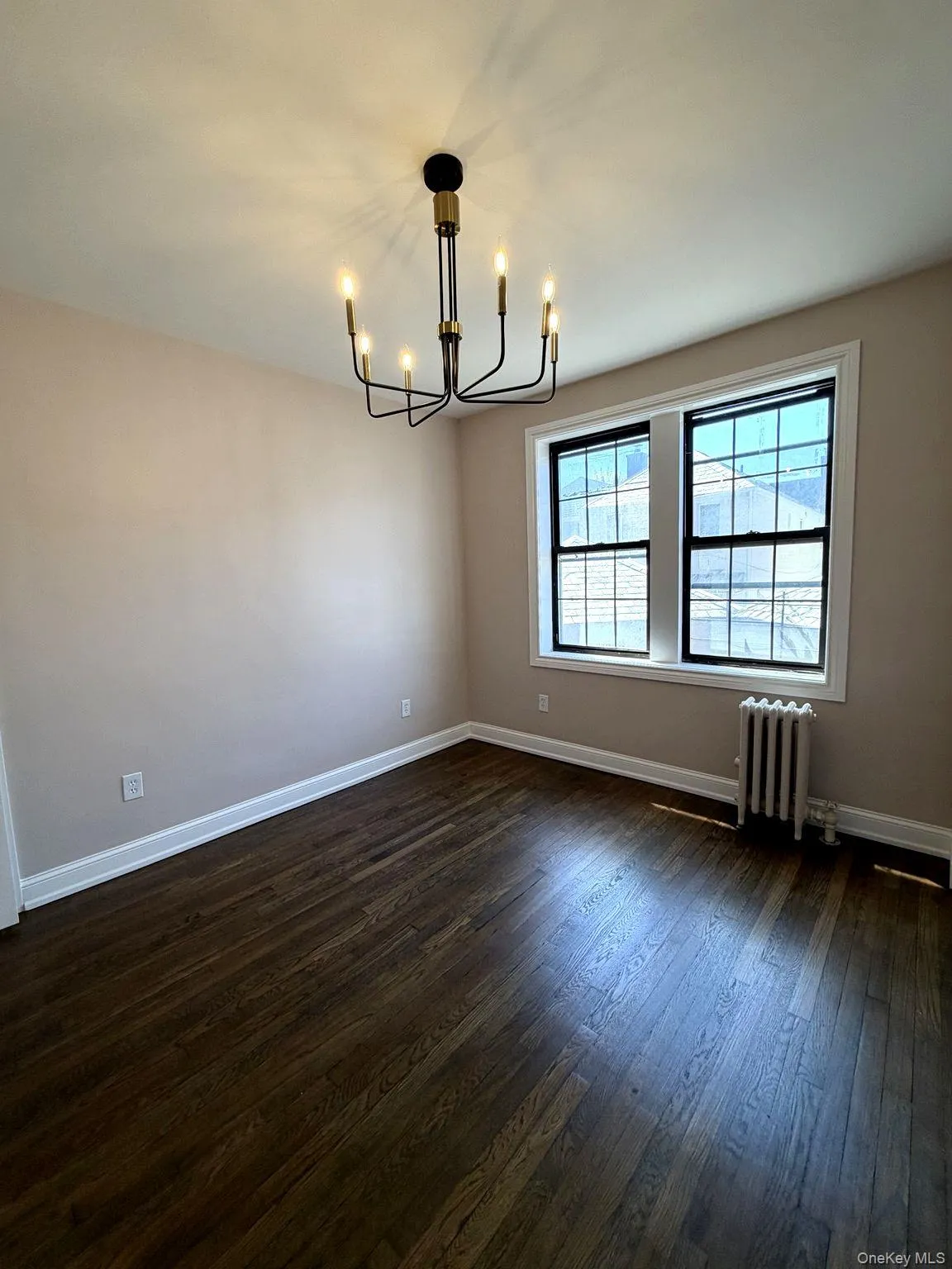 Room featuring dark wood-finish flooring, a modern multi-arm chandelier, and neutral-toned walls Room featuring dark wood-finish flooring, a modern multi-arm chandelier, and neutral-toned walls