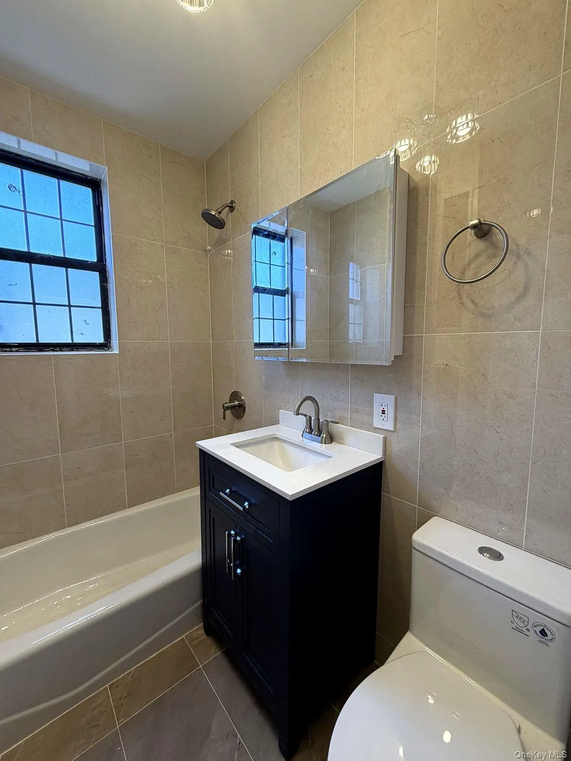 Totally rent Tiled bathroom featuring a dark wood-finish vanity with an integrated white sink and chrome faucet, a mirrored medicine cabinet, and a window and tub Totally rent Tiled bathroom featuring a dark wood-finish vanity with an integrated white sink and chrome faucet, a mirrored medicine cabinet, and a window and tub