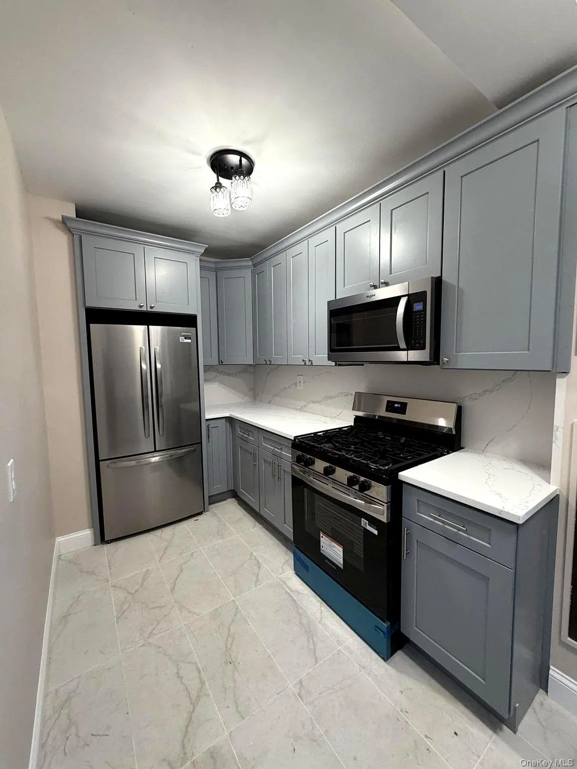 Kitchen featuring light gray shaker-style cabinetry with crown molding, stainless steel appliances, white countertops, and a complementary tile backsplash Kitchen featuring light gray shaker-style cabinetry with crown molding, stainless steel appliances, white countertops, and a complementary tile backsplash