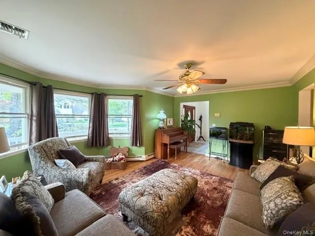 Sunlit living space featuring a bay window, hardwood-style flooring, crown molding, and a ceiling fan with integrated lighting Sunlit living space featuring a bay window, hardwood-style flooring, crown molding, and a ceiling fan with integrated lighting