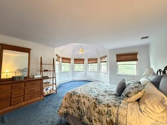 Room featuring a vaulted ceiling with a built-in fan, blue carpeting, and a bay window area with multiple windows Room featuring a vaulted ceiling with a built-in fan, blue carpeting, and a bay window area with multiple windows