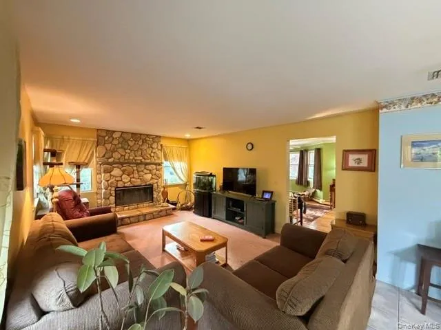 Spacious living area featuring a prominent stone fireplace, recessed lighting, and an open entryway to an additional room Spacious living area featuring a prominent stone fireplace, recessed lighting, and an open entryway to an additional room