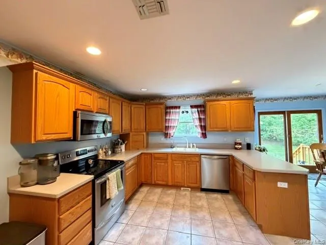 Kitchen featuring extensive wood cabinetry, stainless steel appliances, light countertops, and tile flooring Kitchen featuring extensive wood cabinetry, stainless steel appliances, light countertops, and tile flooring