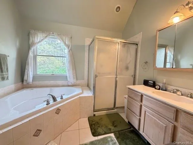Bathroom featuring a corner soaking tub, a separate shower with sliding glass doors, a vanity with dual sinks, and a window with natural light Bathroom featuring a corner soaking tub, a separate shower with sliding glass doors, a vanity with dual sinks, and a window with natural light