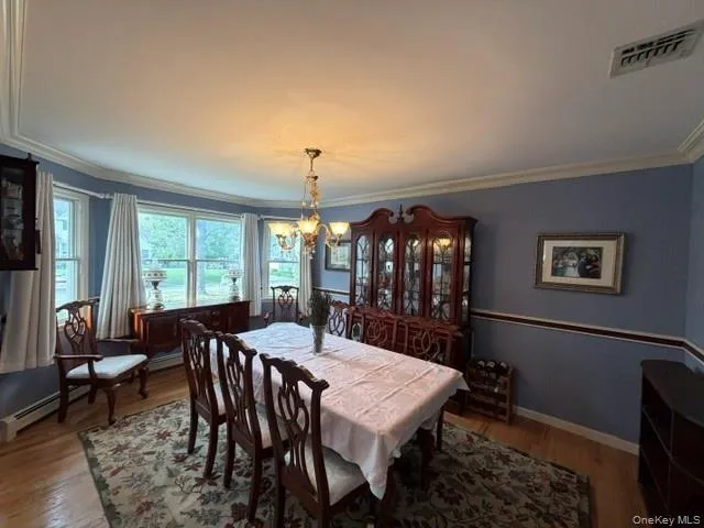 Formal dining area featuring light blue walls with chair rail molding, wood-finish flooring, and a multi-panel bay window Formal dining area featuring light blue walls with chair rail molding, wood-finish flooring, and a multi-panel bay window