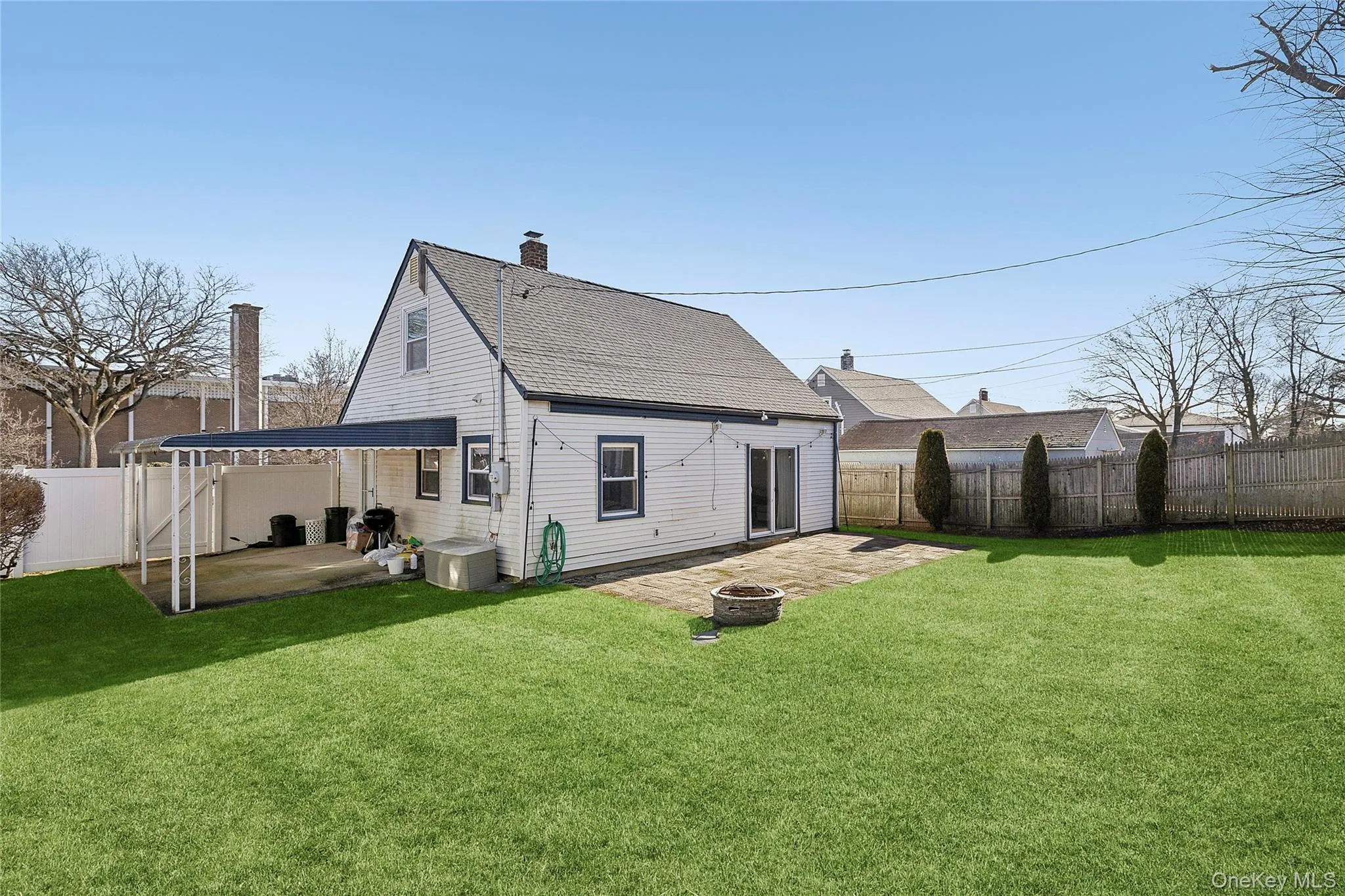 Spacious grassy backyard with a paved patio area, featuring a fire pit Spacious grassy backyard with a paved patio area, featuring a fire pit