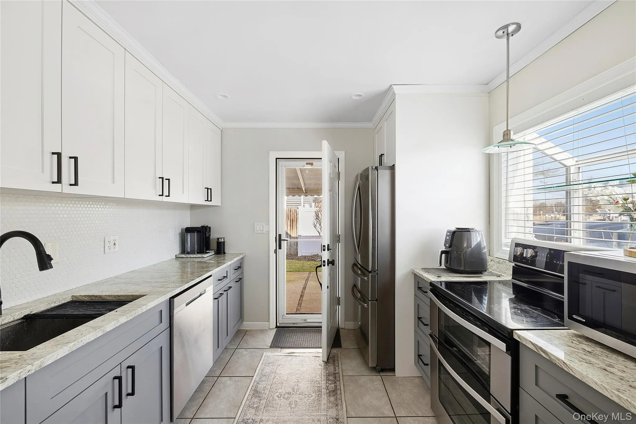 Updated kitchen featuring two-tone cabinetry, light-toned countertops, and a white honeycomb tile backsplash Updated kitchen featuring two-tone cabinetry, light-toned countertops, and a white honeycomb tile backsplash