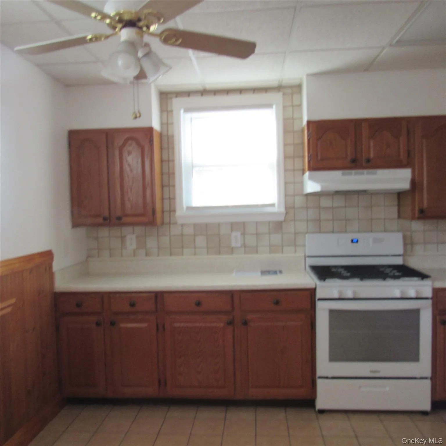 Kitchen with white range with gas stovetop, brown cabinetry, light countertops, ceiling fan, and exhaust hood Kitchen with white range with gas stovetop, brown cabinetry, light countertops, ceiling fan, and exhaust hood