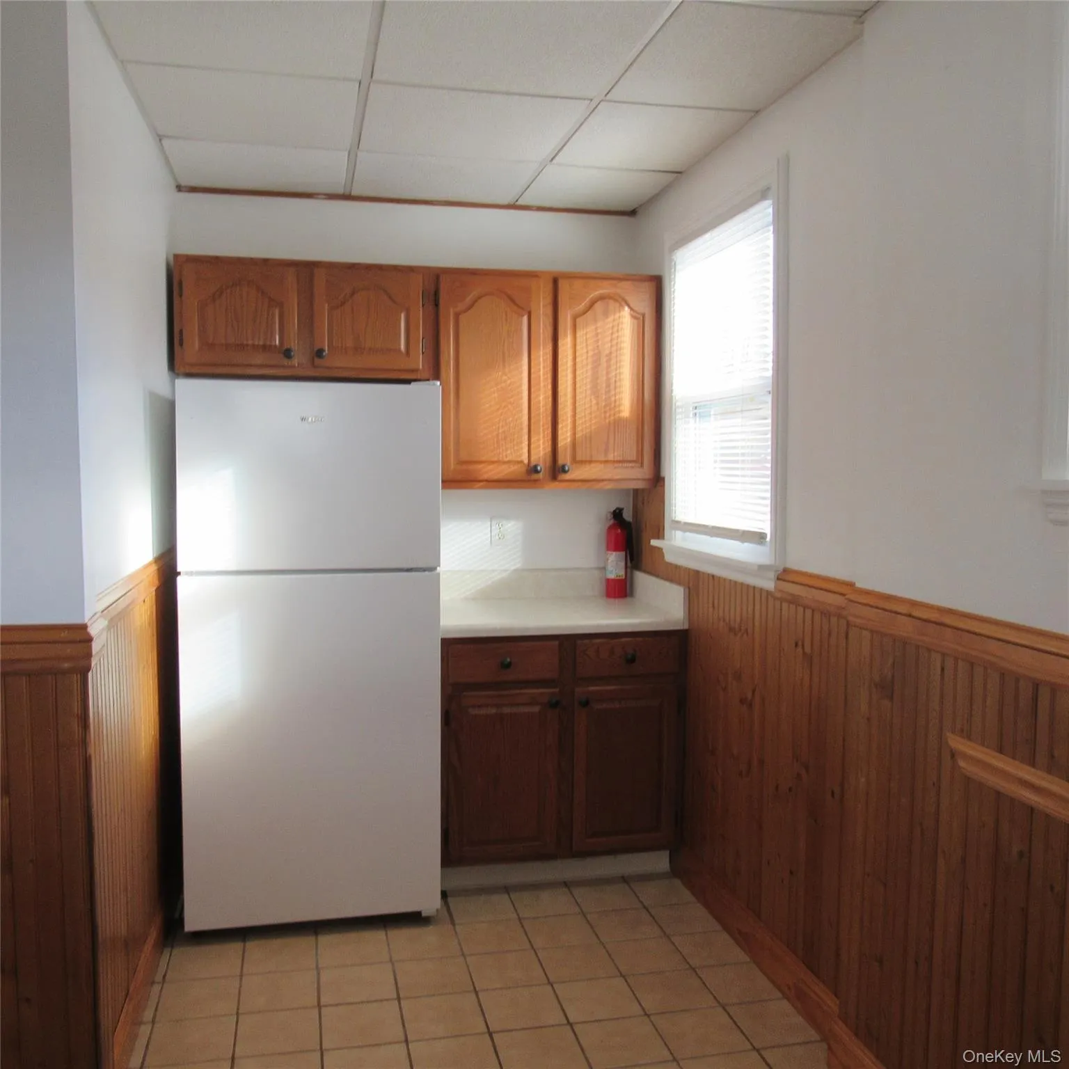 Kitchen with panelled walls, freestanding refrigerator, light countertops, and brown cabinetry Kitchen with panelled walls, freestanding refrigerator, light countertops, and brown cabinetry