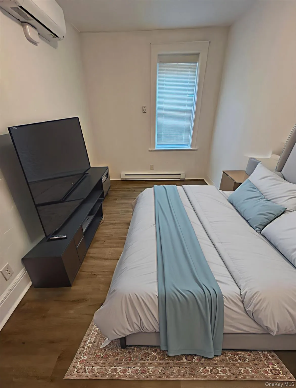 Bedroom featuring wood finished floors, a wall mounted AC, and a baseboard heating unit Bedroom featuring wood finished floors, a wall mounted AC, and a baseboard heating unit