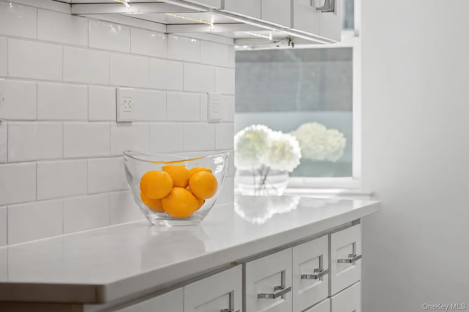 Sleek kitchen finishes include glossy subway tile, under-cabinet lighting, white cabinetry, and a quartz countertop Sleek kitchen finishes include glossy subway tile, under-cabinet lighting, white cabinetry, and a quartz countertop