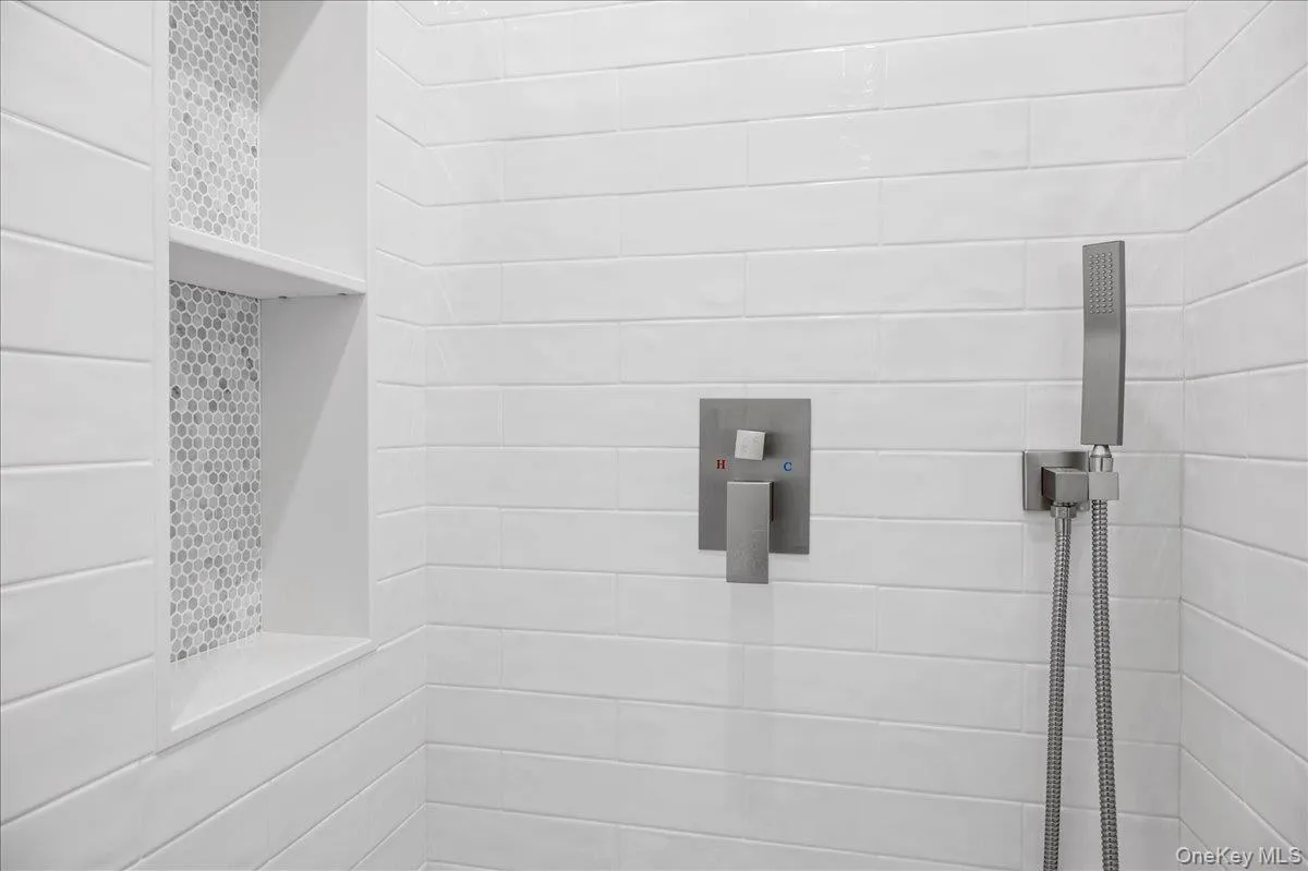 Walk-in shower features glossy subway tile, built-in niche shelving, and a sleek handheld shower fixture. Walk-in shower features glossy subway tile, built-in niche shelving, and a sleek handheld shower fixture.