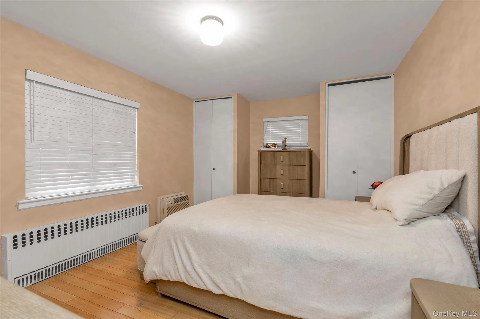 Bedroom featuring wood-finish flooring, two windows with blinds, and two integrated closets with bi-fold doors Bedroom featuring wood-finish flooring, two windows with blinds, and two integrated closets with bi-fold doors