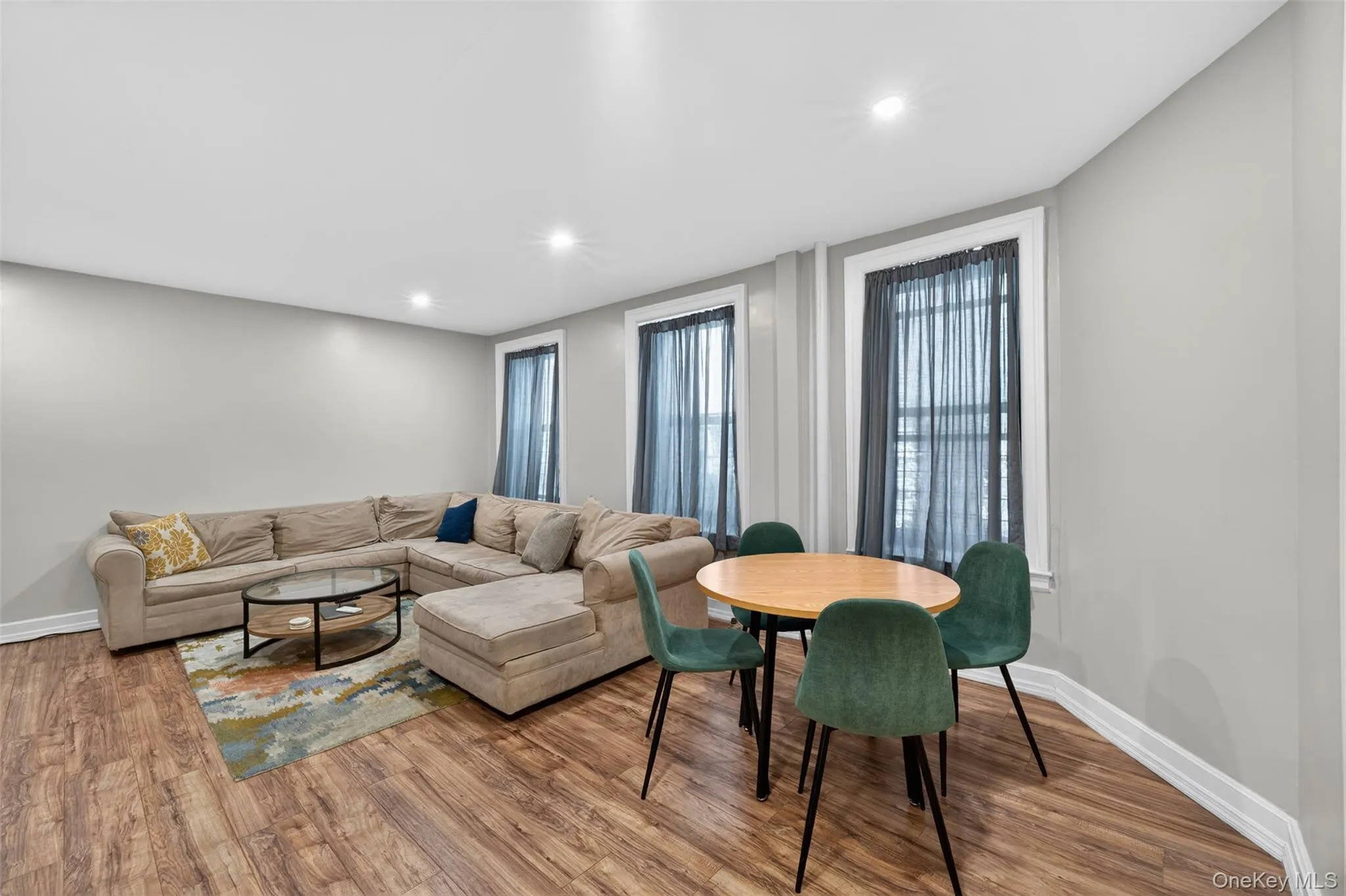 Open-concept living area featuring wood-finish flooring, recessed lighting, and light gray wall paint Open-concept living area featuring wood-finish flooring, recessed lighting, and light gray wall paint