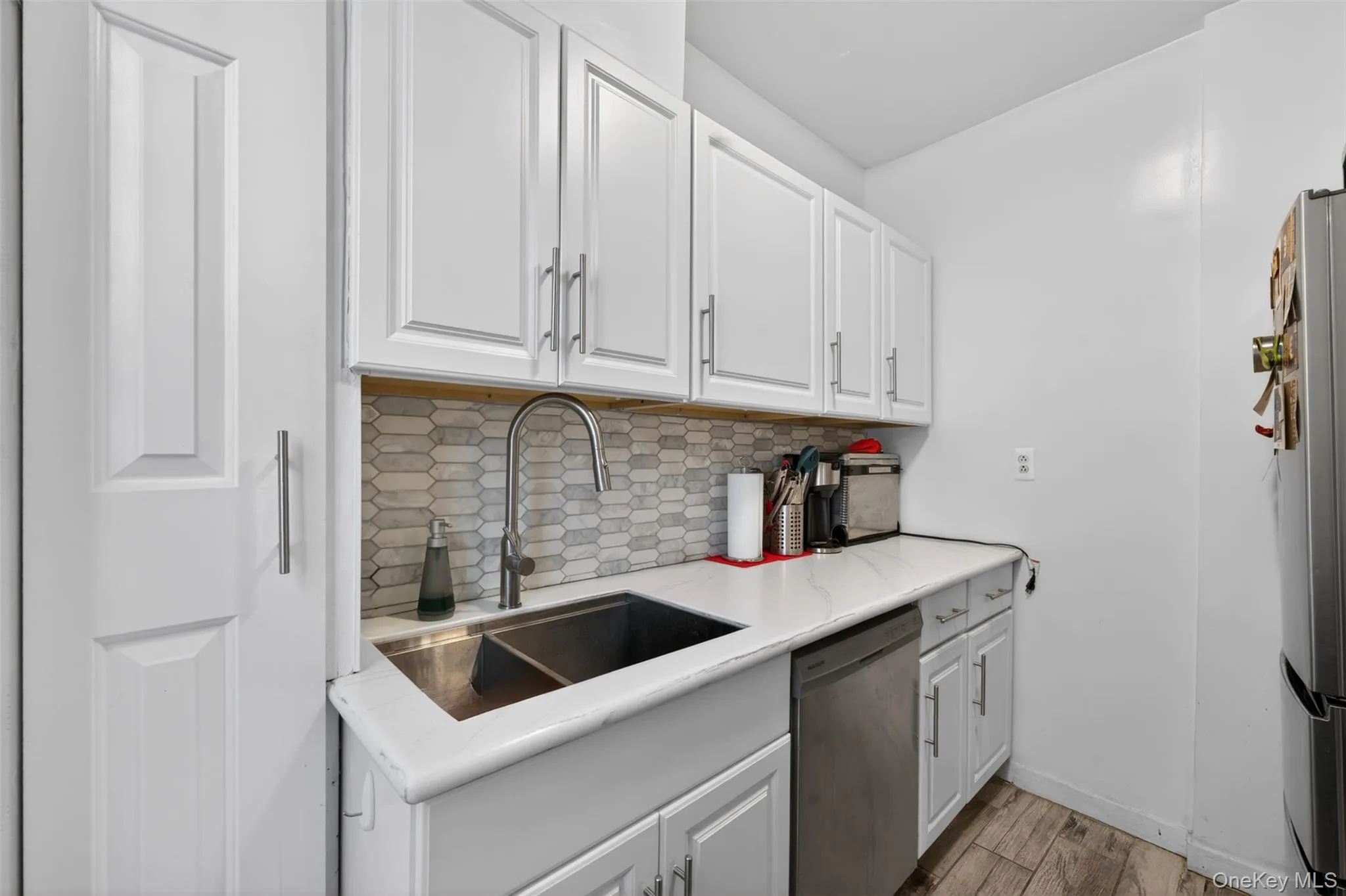 Kitchen featuring white cabinetry, a dual basin stainless steel sink with a gooseneck faucet, a light-toned countertop, and a patterned tile backsplash Kitchen featuring white cabinetry, a dual basin stainless steel sink with a gooseneck faucet, a light-toned countertop, and a patterned tile backsplash