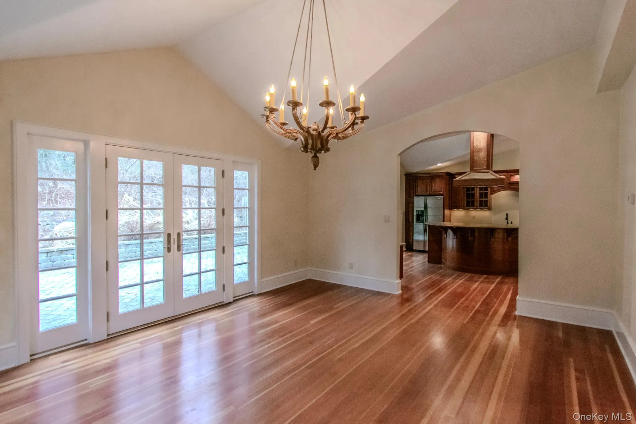 Unfurnished dining area featuring hardwood / wood-style floors, high vaulted ceiling, french doors, and an inviting chandelier Unfurnished dining area featuring hardwood / wood-style floors, high vaulted ceiling, french doors, and an inviting chandelier