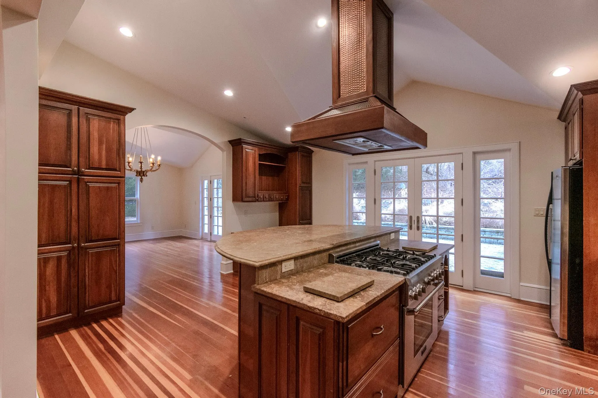 Kitchen with french doors, stainless steel appliances, lofted ceiling, and island range hood Kitchen with french doors, stainless steel appliances, lofted ceiling, and island range hood