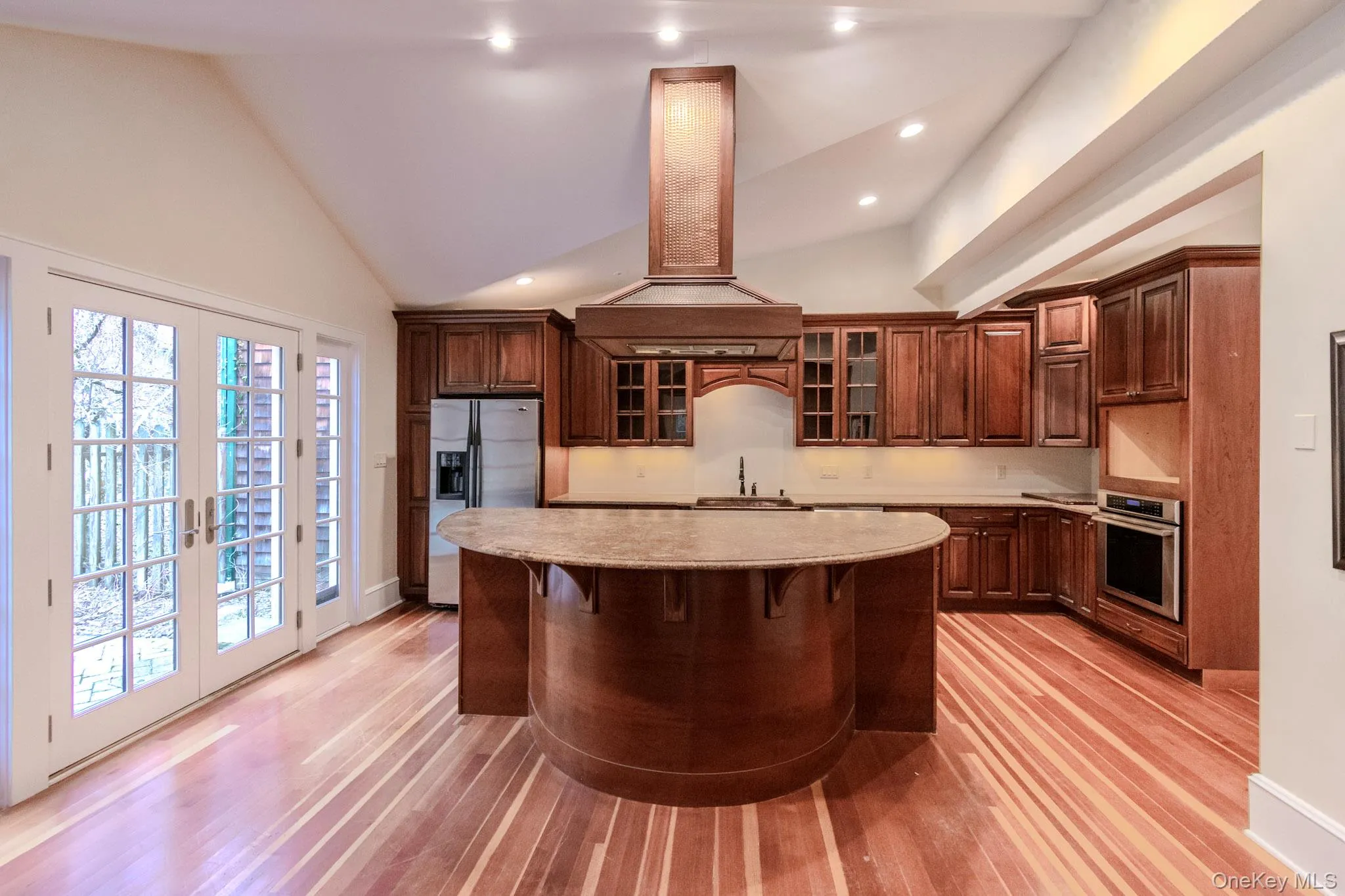 Kitchen featuring island exhaust hood, french doors, stainless steel appliances, high vaulted ceiling, and a center island Kitchen featuring island exhaust hood, french doors, stainless steel appliances, high vaulted ceiling, and a center island