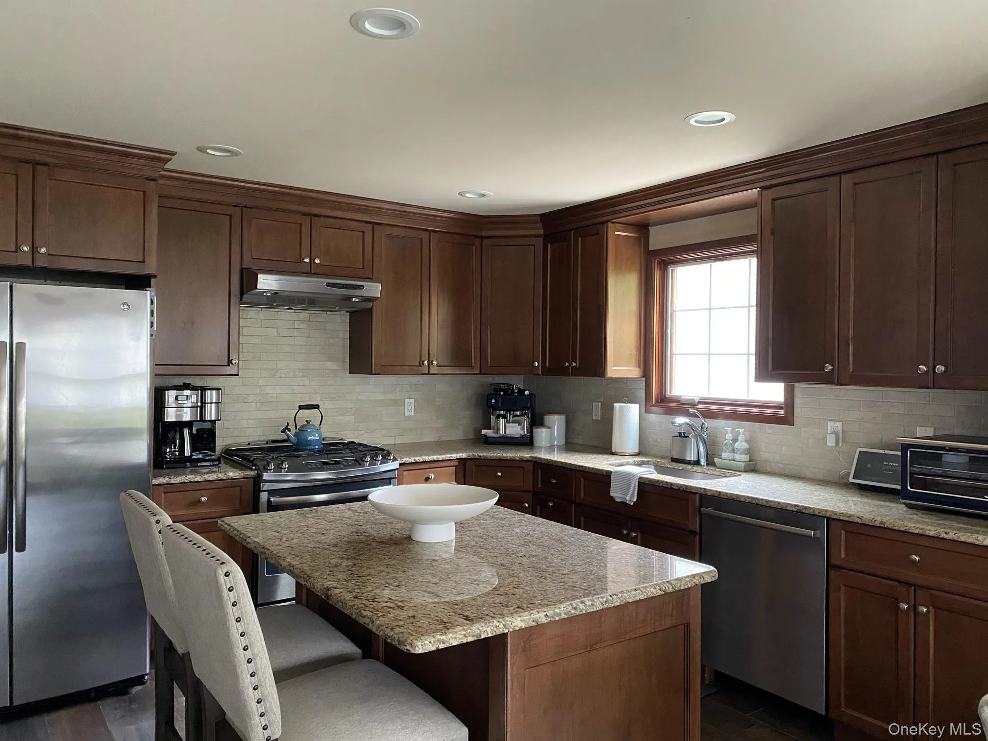 Kitchen featuring rich wood cabinetry, stainless steel appliances, a center island with a granite-style countertop, and recessed lighting Kitchen featuring rich wood cabinetry, stainless steel appliances, a center island with a granite-style countertop, and recessed lighting