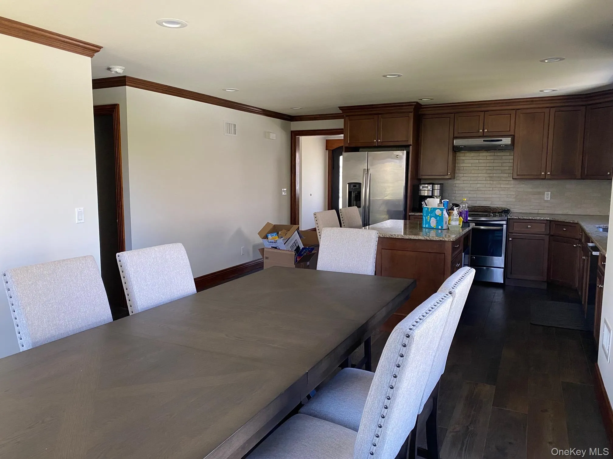 Open-concept kitchen and dining area featuring dark wood-finish flooring, recessed lighting, wood cabinetry, and a subway tile backsplash Open-concept kitchen and dining area featuring dark wood-finish flooring, recessed lighting, wood cabinetry, and a subway tile backsplash