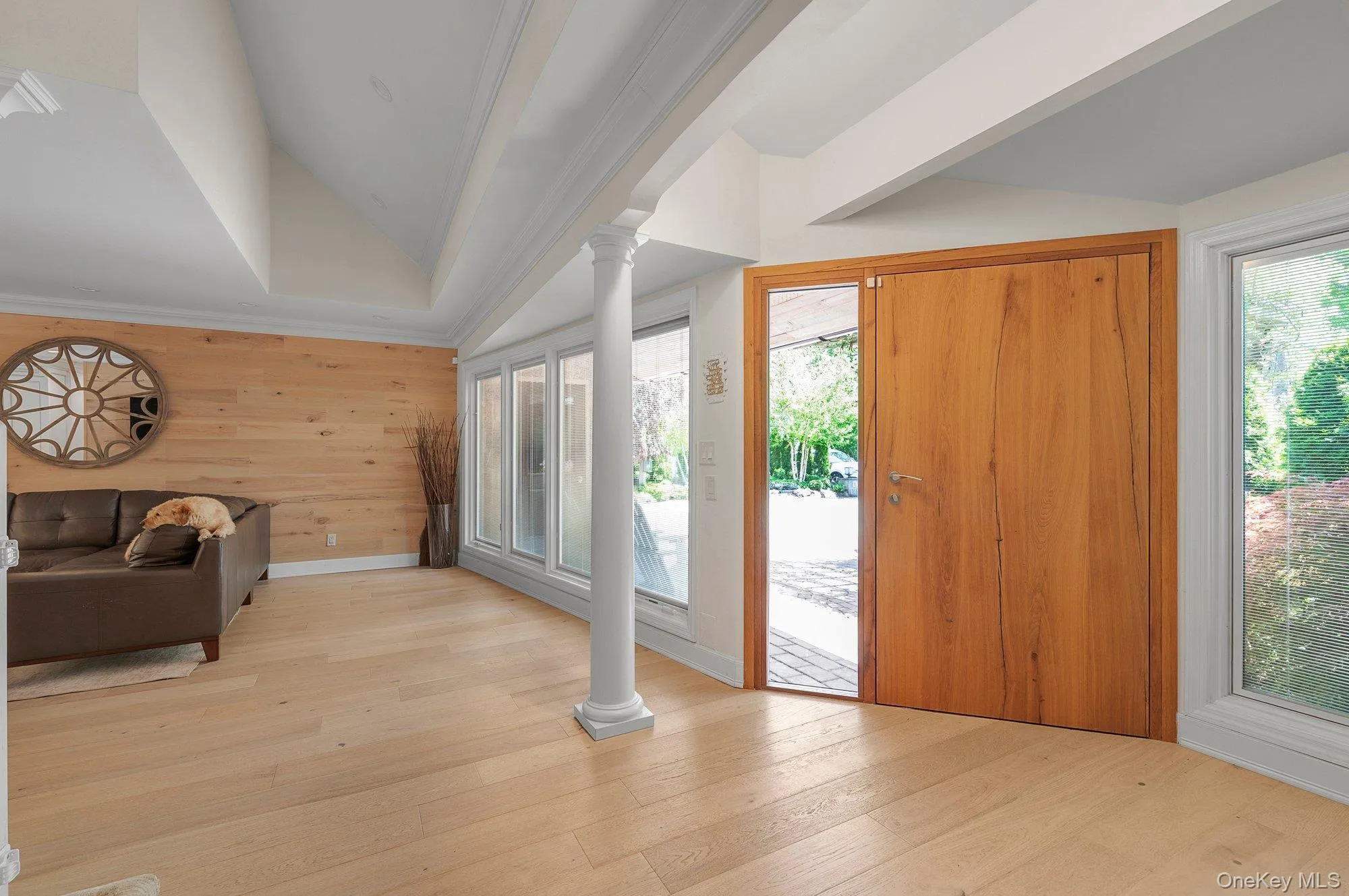 Spacious entryway featuring light wood-finish flooring, a natural wood paneled wall, and a wood entry door with a sidelight Spacious entryway featuring light wood-finish flooring, a natural wood paneled wall, and a wood entry door with a sidelight