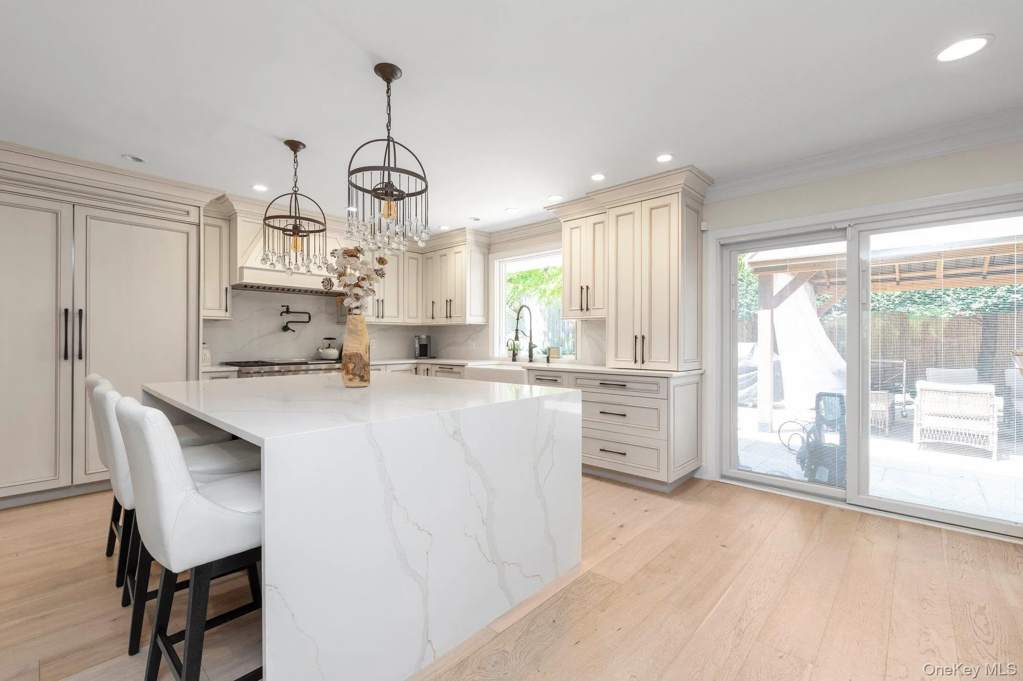 Spacious kitchen featuring a waterfall-edge island, light wood-finish flooring, recessed lighting, and a paneled refrigerator Spacious kitchen featuring a waterfall-edge island, light wood-finish flooring, recessed lighting, and a paneled refrigerator