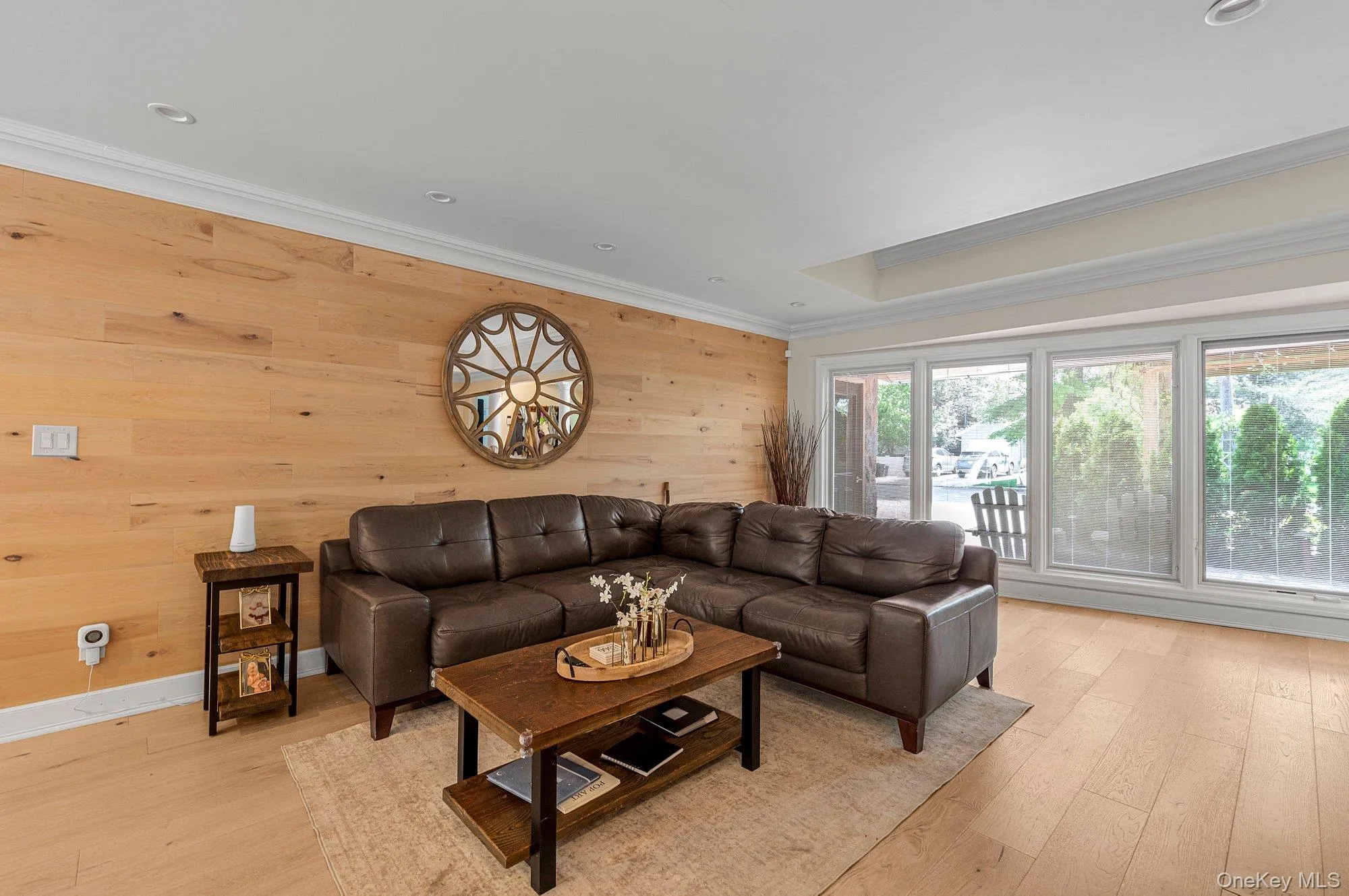 Spacious living area featuring a light wood-finish accent wall, crown molding, recessed lighting, and large picture windows Spacious living area featuring a light wood-finish accent wall, crown molding, recessed lighting, and large picture windows