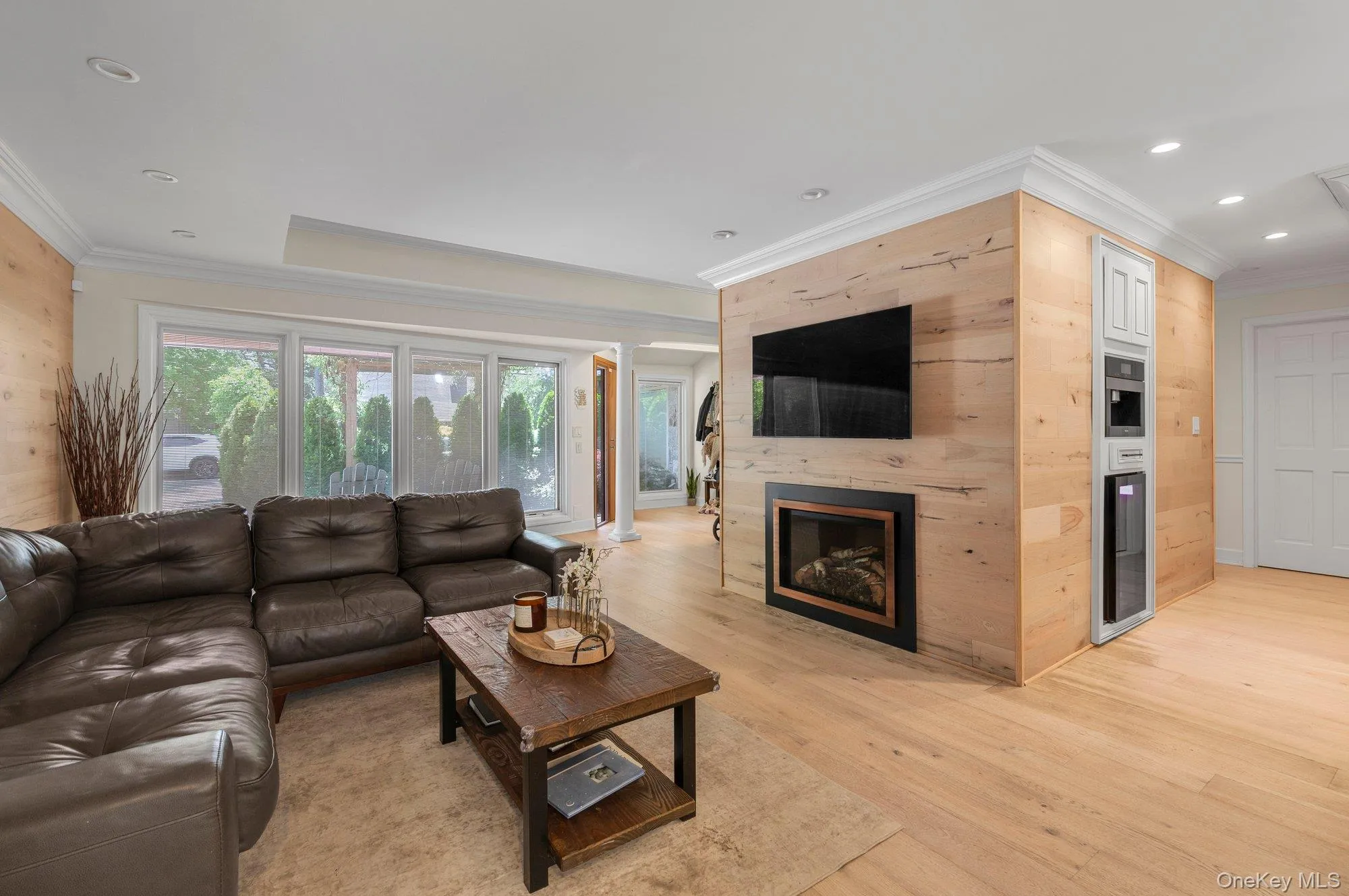 Open-concept living area featuring light wood-finish flooring, a contemporary fireplace with a black surround, and a built-in beverage station Open-concept living area featuring light wood-finish flooring, a contemporary fireplace with a black surround, and a built-in beverage station