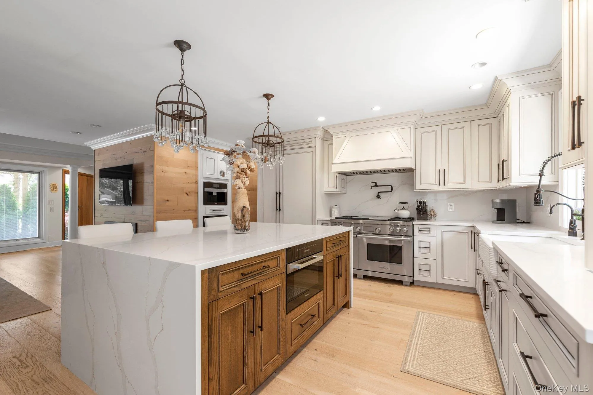Gourmet kitchen featuring a large central island with waterfall countertop, professional-grade stainless steel range, custom cabinetry, light wood-finish flooring, and built-in appliances, Miele coffee unit with wine refrigerator Gourmet kitchen featuring a large central island with waterfall countertop, professional-grade stainless steel range, custom cabinetry, light wood-finish flooring, and built-in appliances, Miele coffee unit with wine refrigerator