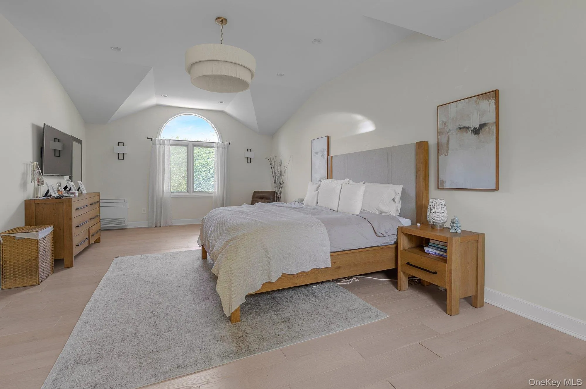 Vaulted ceiling bedroom with a prominent arched window and light wood-finish flooring Vaulted ceiling bedroom with a prominent arched window and light wood-finish flooring