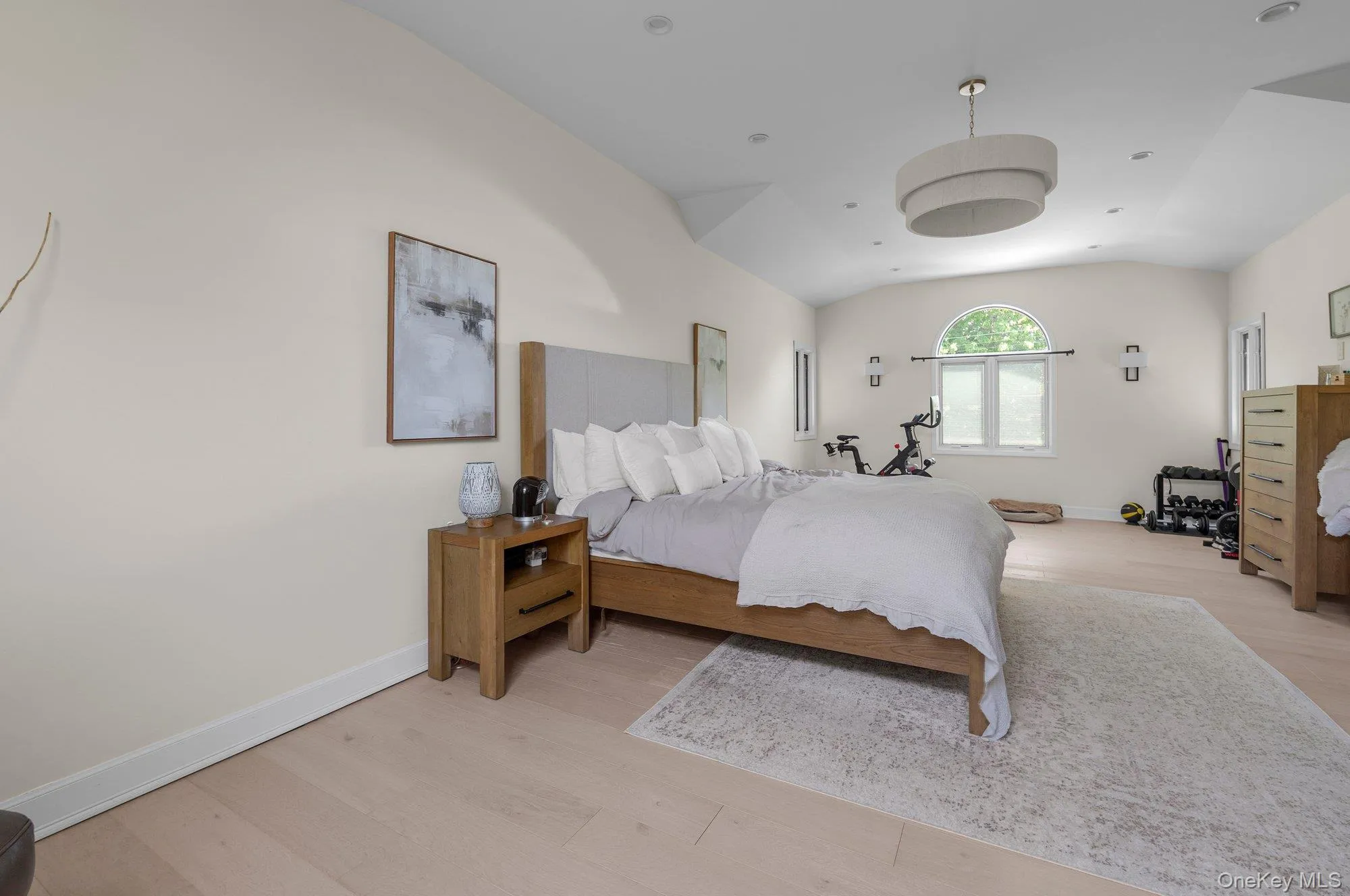 Spacious room featuring wood-finish flooring, vaulted ceilings, and a large arched window Spacious room featuring wood-finish flooring, vaulted ceilings, and a large arched window