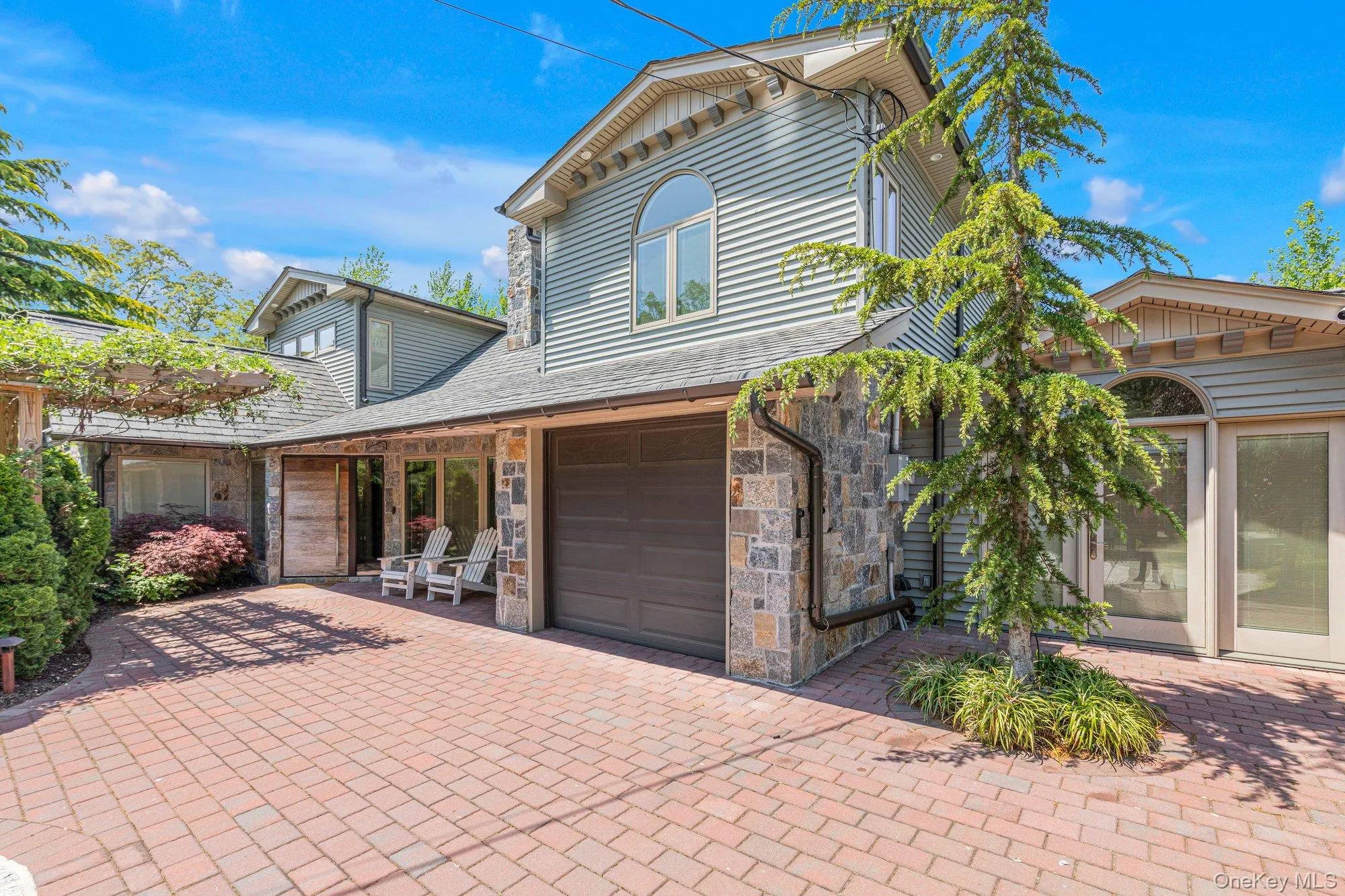Exterior showcasing a red brick paver driveway, stone facade accents, horizontal siding, an arched window, and a pergola-covered entrance Exterior showcasing a red brick paver driveway, stone facade accents, horizontal siding, an arched window, and a pergola-covered entrance
