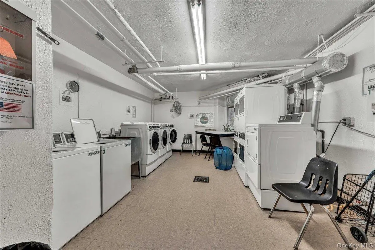 Communal laundry room with separate washer and dryer, stacked washer and clothes dryer, light floors, a textured ceiling, and a textured wall Communal laundry room with separate washer and dryer, stacked washer and clothes dryer, light floors, a textured ceiling, and a textured wall
