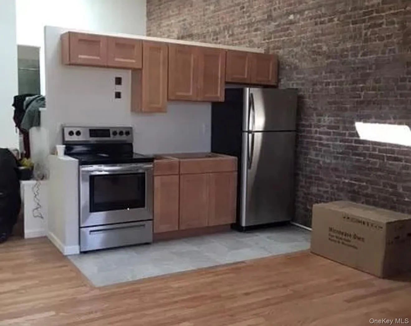 Kitchen with stainless steel appliances, light wood finished floors, and brick wall Kitchen with stainless steel appliances, light wood finished floors, and brick wall