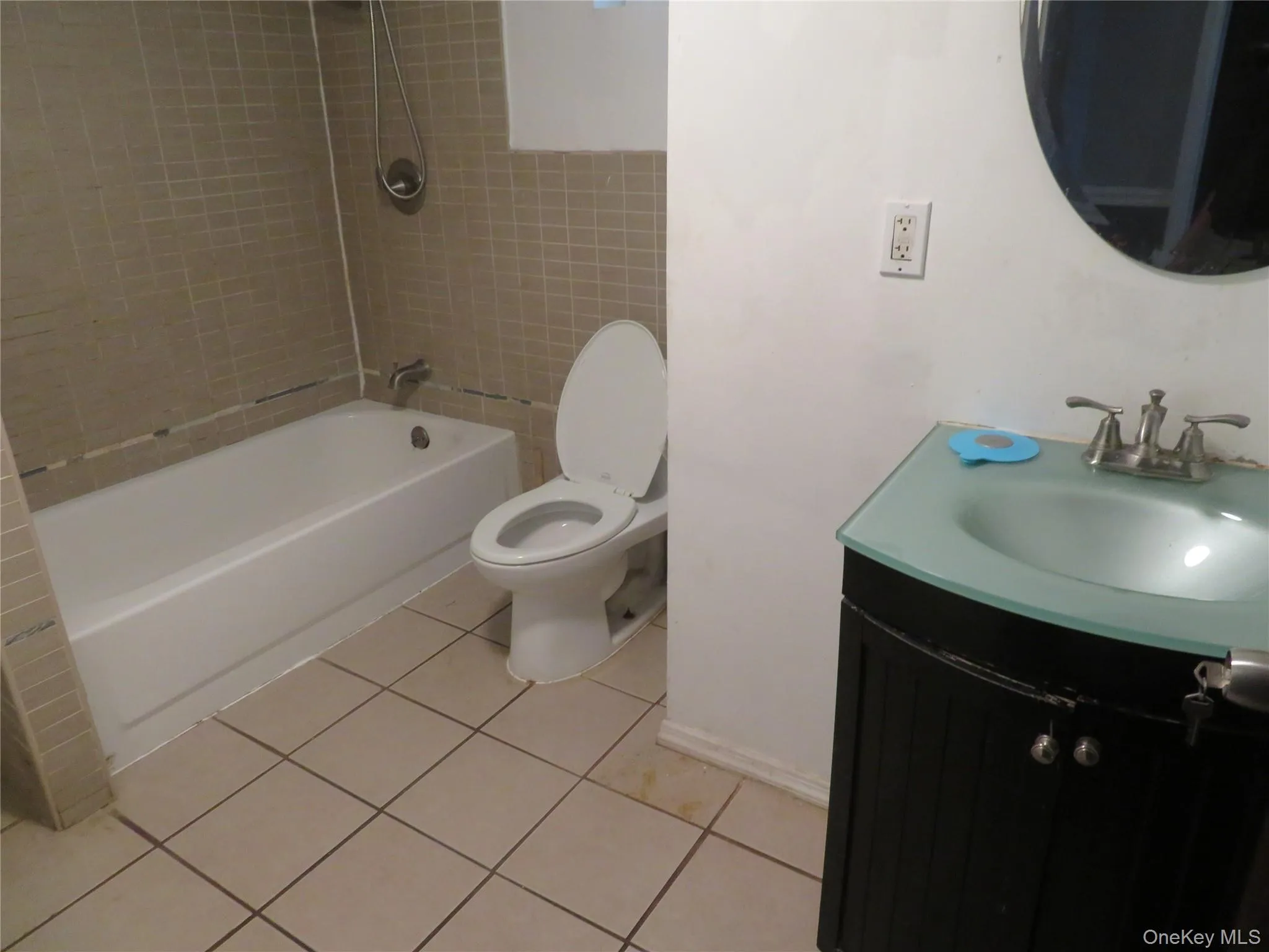 Bathroom featuring a white bathtub, ceramic wall tiling, floor tiling, a white toilet, and a black vanity with a light-colored basin Bathroom featuring a white bathtub, ceramic wall tiling, floor tiling, a white toilet, and a black vanity with a light-colored basin